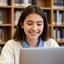 Lylyana Loacker, college student, smiling with laptop in a library